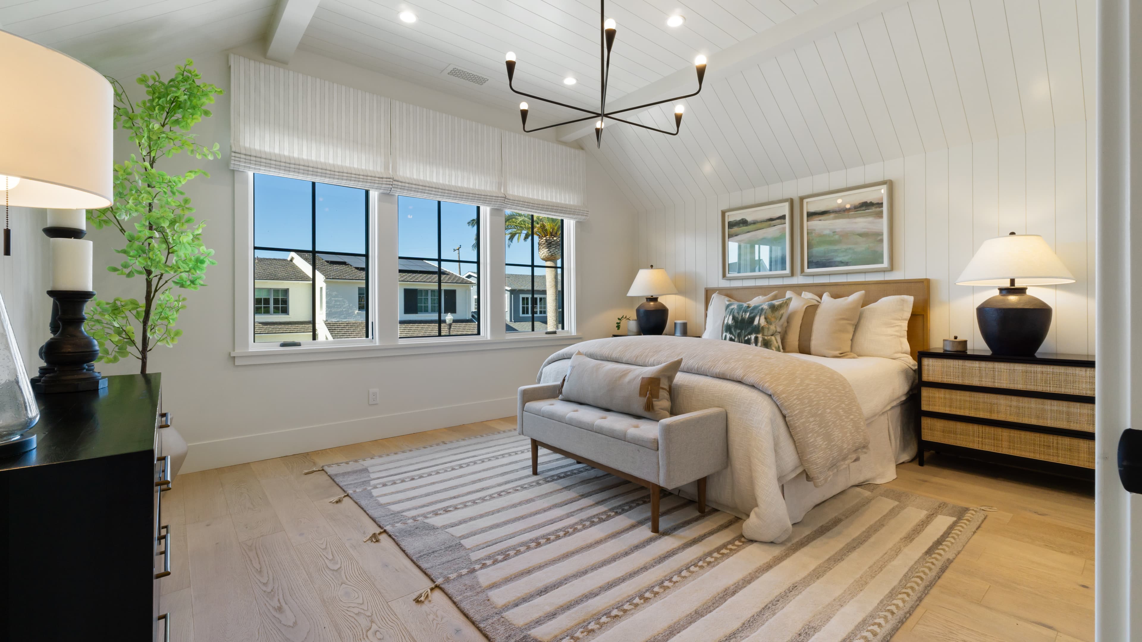Master bedroom with sloped ceiling, large windows, and a chandelier hanging over the king bed.
